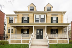 Yellow 19th century house with front porch and black shutters.