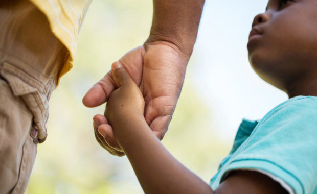 child looking up and holding unseen adult's hand