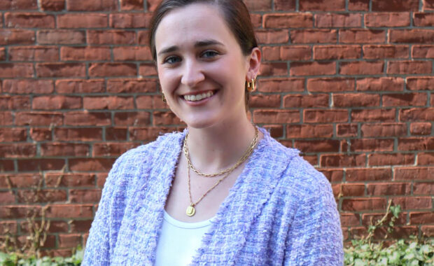 Sarah Berton light gray sweater, standing against brick wall
