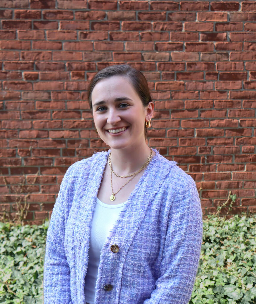 Sarah Berton light gray sweater, standing against brick wall