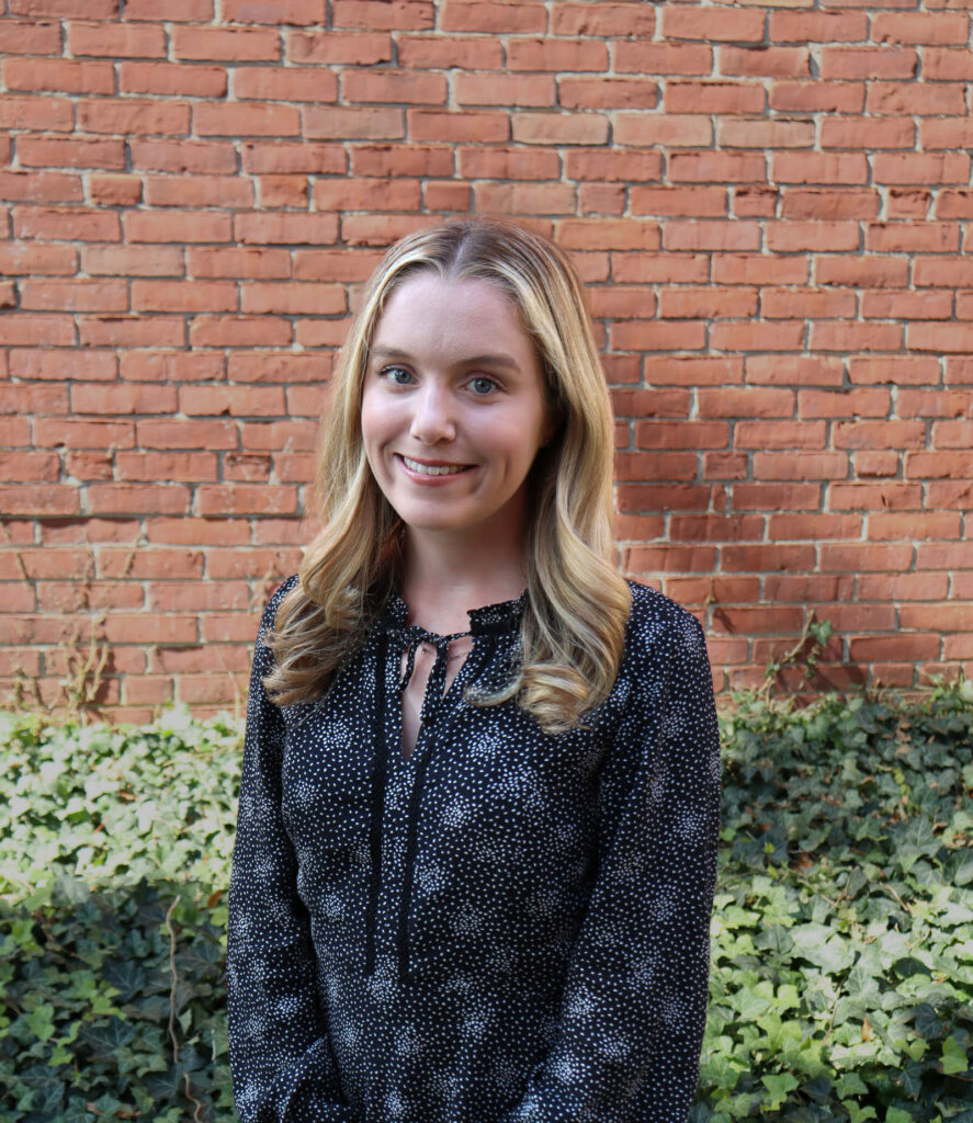 Sophie Lenihan dark long-sleeved shirt with gray flowers standing against brick wall