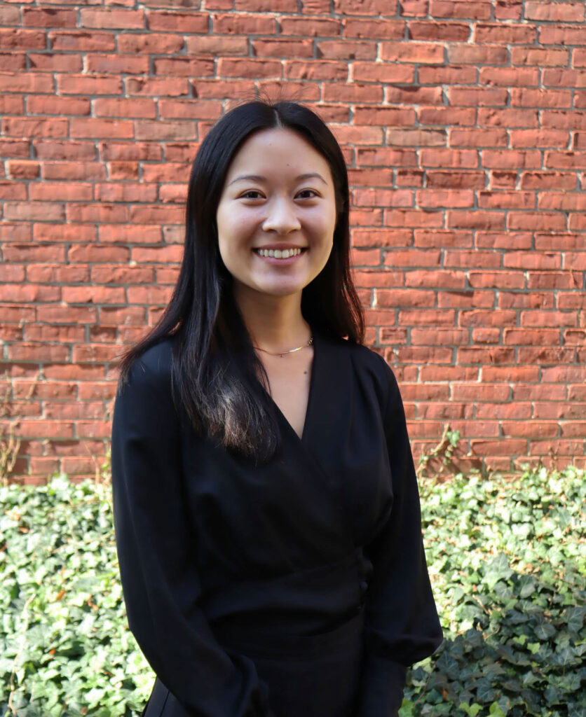 Sunah Chang black long-sleeved shirt standing against brick wall