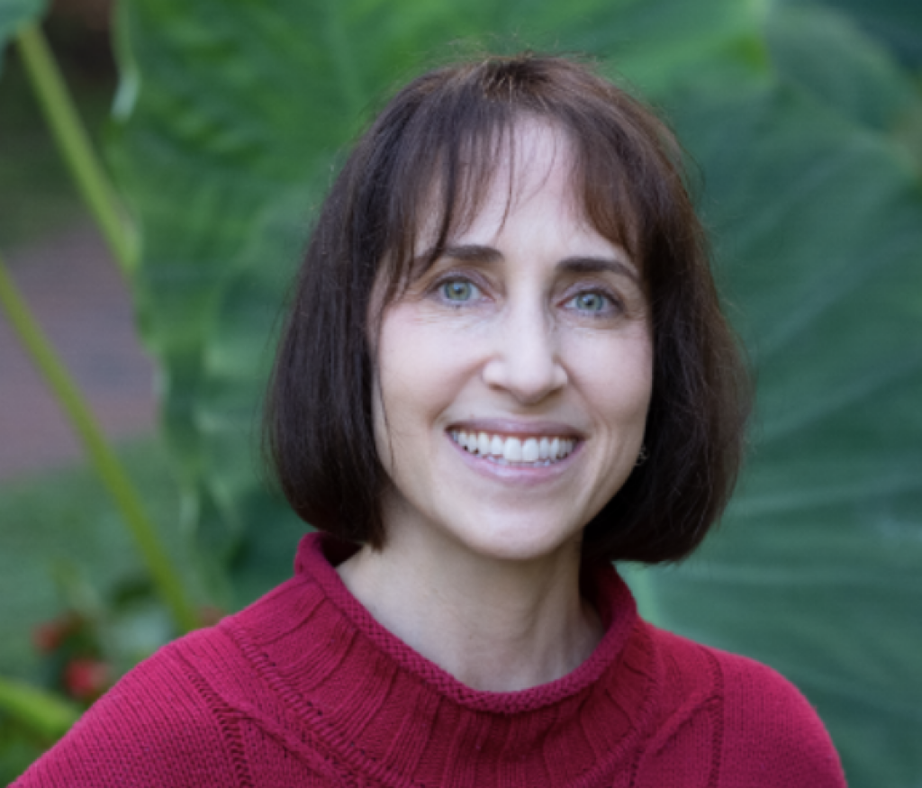 R. Belin headshot, red sweater, green trees in the background