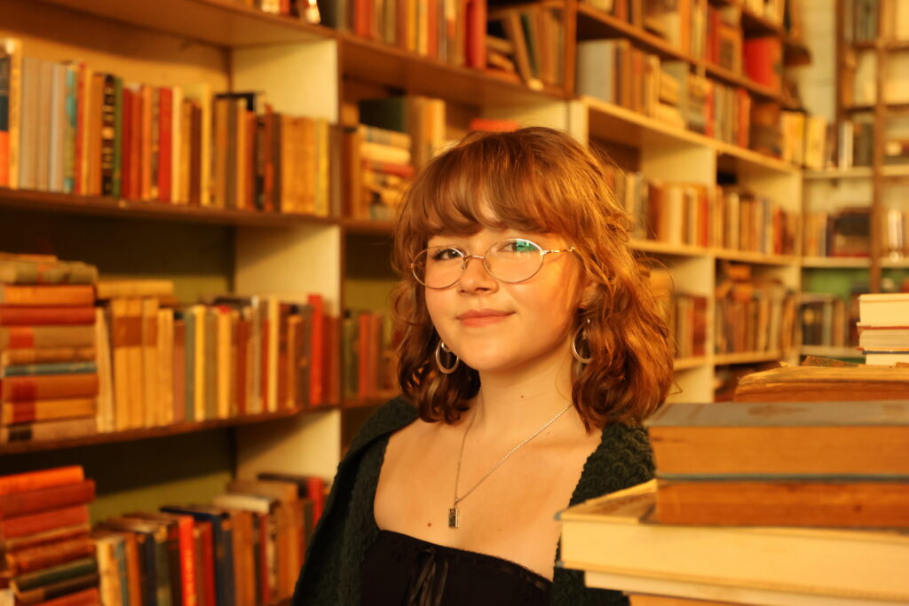 Georgie Farmer standing in front of bookshelves, wearing dark top.