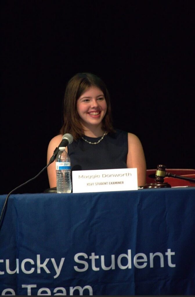 Maggie Donworth speaking at panelist table with microphone, wearing a dark top.