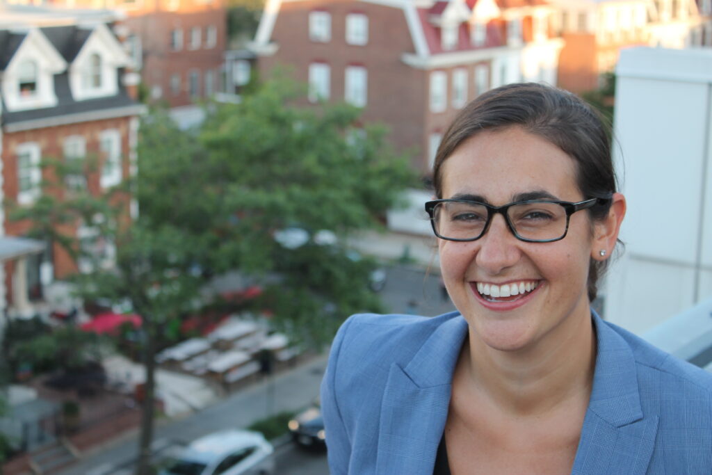 Jillian Lenson headshot, light blue blazer, with brick building sky line behind/below her.