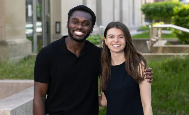 Cordy McJunkins in a black t-shirt and Wesley Streicher in a black t-shirt standing in front of HLS building.